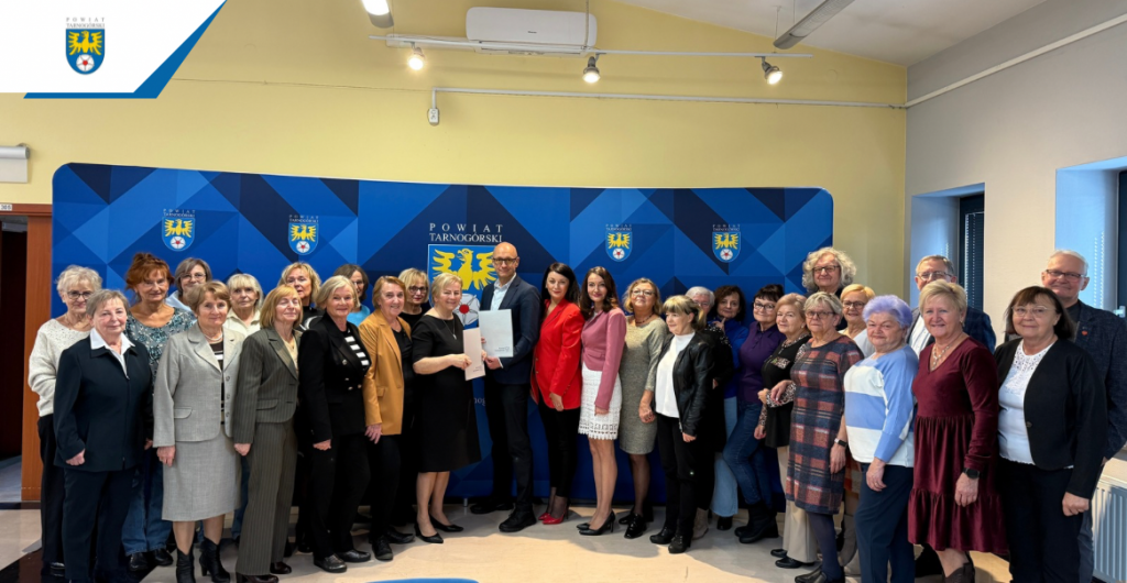 grupa osób, pozuje do zdjęcia przy ściance z herbem powiatu tarnogórskiego