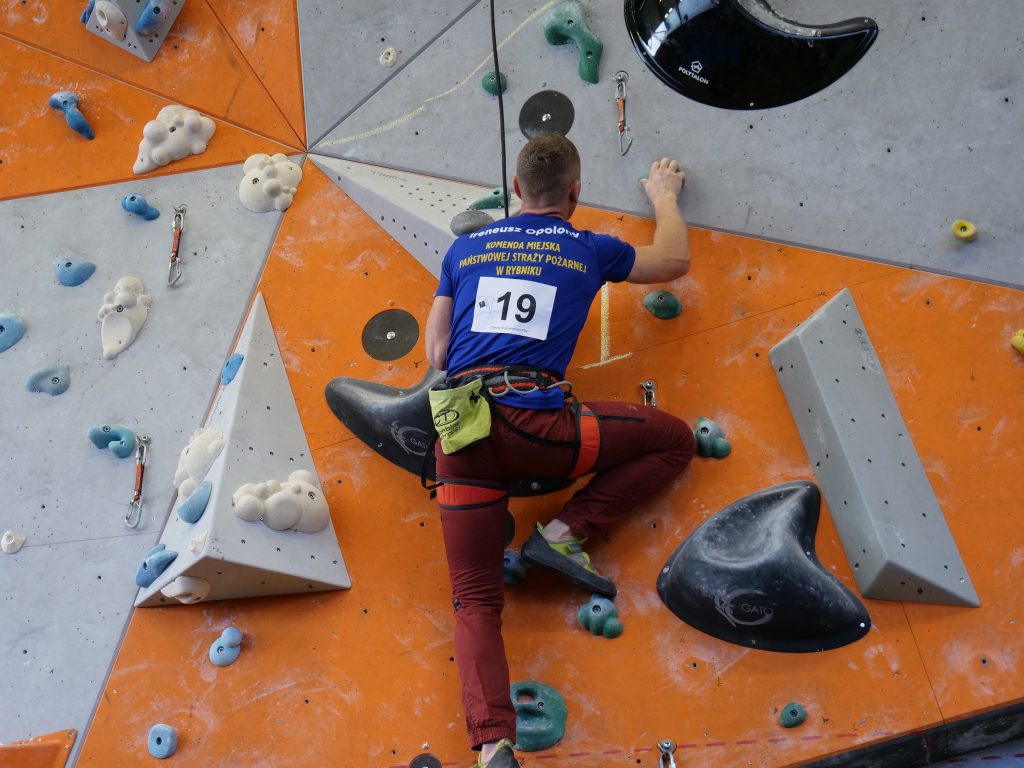 mężczyzna, w stroju sportowym, wspina się po ściance wspinaczkowej