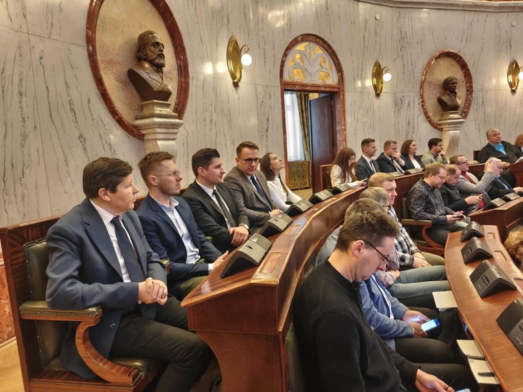 grupa osób uczestniczących na spotkaniu w sali posiedzeń sejmowych, w tle ściana i rzeźby 