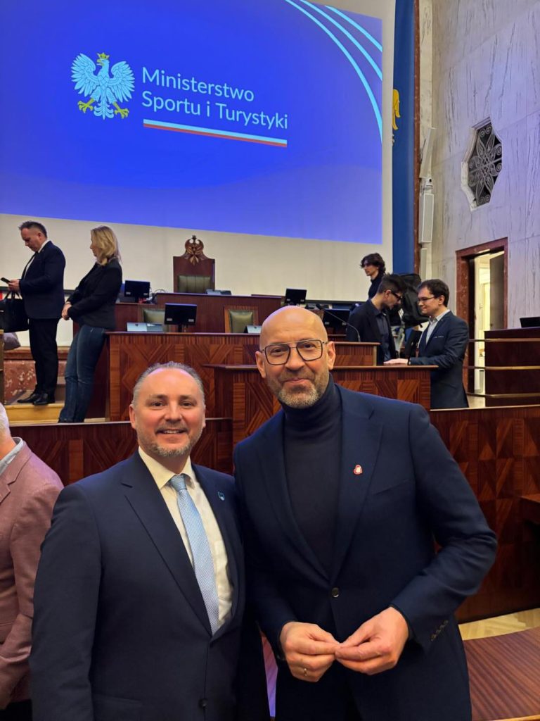 dwóch mężczyzn, pozują do zdjęcia, w tle sala sejmowa, duży ekran multimedialny